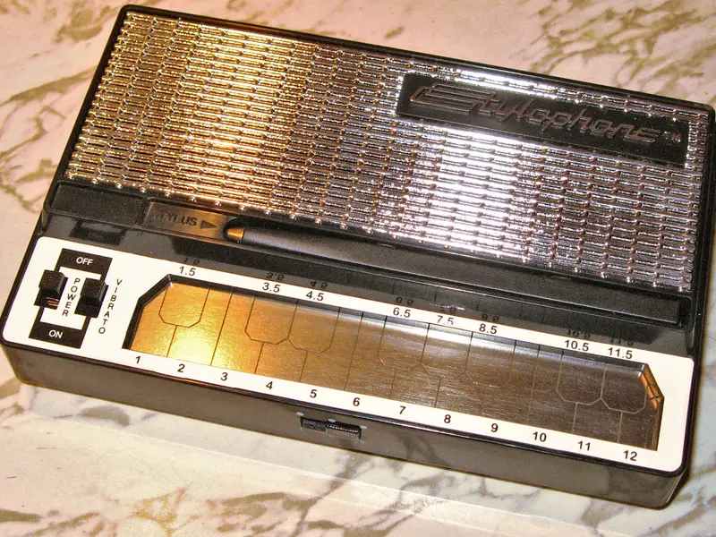 A modern Dubreq Stylophone with its stylus resting on the metal keyboard